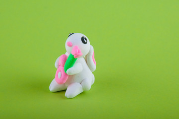 Cute white bunny madeof modelling clay holding pink flowers on green background