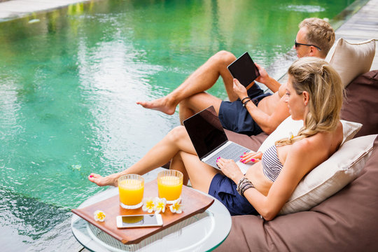 Couple working with computers while on vacation by the pool