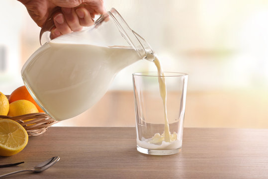 Filling glass of milk with jug in white kitchen