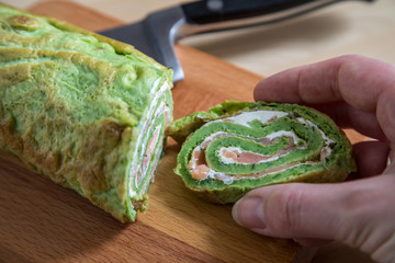 Frau nimmt Spinat Pfannkuchenrolle mit Räucherlachs und Frischkäse von Holzbrett