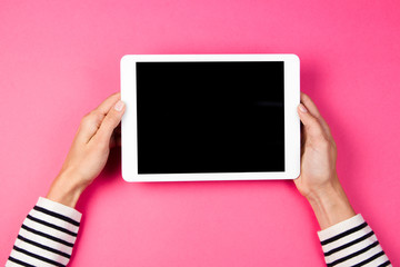 Woman's hands with tablet computer on pink background.