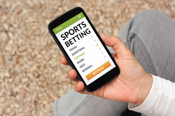 Hand holding smart phone with sports betting concept on screen. All screen content is designed by me