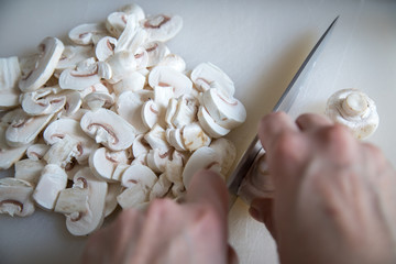 Frau schneidet weiße Champignons mit Messer auf Schneidebrett in Küche