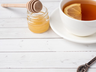 Herbal black tea in a white Cup, honey in a jar of fresh lemon on white wooden background