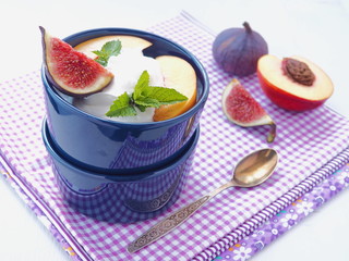 Close up of fruit salad dressed with whipped cream. Fresh figs and other summer fruits upon light grey wooden table. Selective focus.