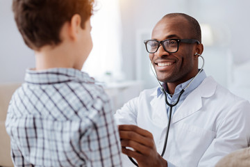 Stethoscope exam. Attractive cheerful male doctor listening to boy while putting on glasses and using stethoscope - Powered by Adobe