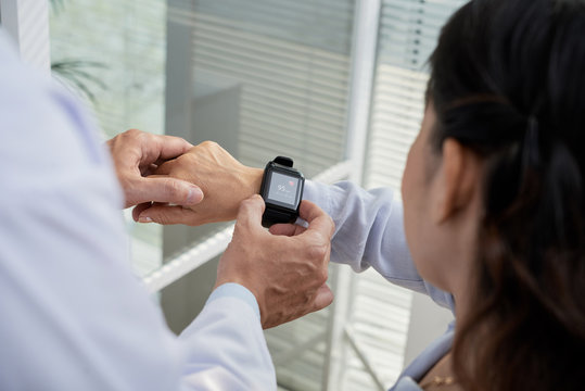 Over shoulder view of friendly therapist showing his senior patient how to check heart rate with help of smartwatch, close-up shot