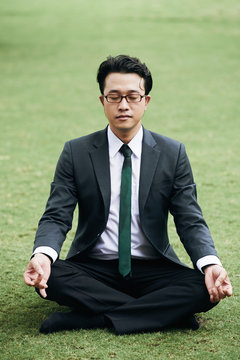 Portrait of Asian businessman in sut meditating on green grass in park