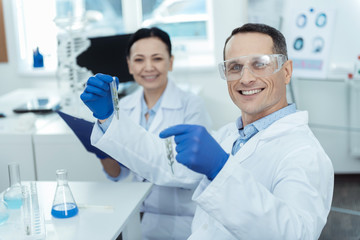 laboratory analysis. Cheerful professional lab workers holding test tubes while conducting a reseacrh