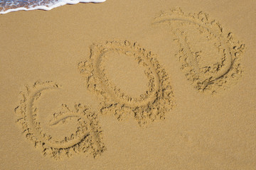 Handwriting words god on sand of beach