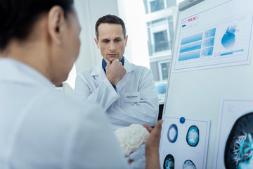 What to do. Thoughtful doctor holding a brain model while dealing with neurosurgery