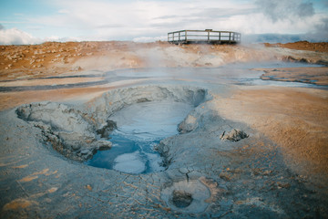 beautiful scenic view of geothermal hot springs with steam and wooden bridge behind, iceland