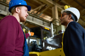 Side view portrait of factory worker talking to young Middle-Eastern engineer
about heavy vehicles