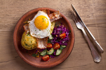 Baked potato in jacket loaded with cheese and topped with bacon and fried egg on plate with vegetables. Stuffed potato with topping. View from above, top, overhead