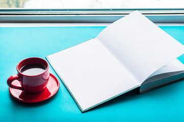 red cup of coffee and a book on a blue background by the window. concept morning at home. Mockup