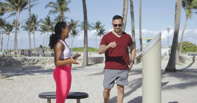 Young black girl helping young sportive man and motivating while training together on beach. 