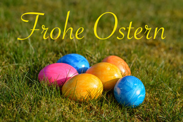 Happy Easter in German with several colorful Easter eggs lying on grass