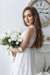 Gorgeous brunette with long hair holds large bouquet of tulips standing before a wall with watch