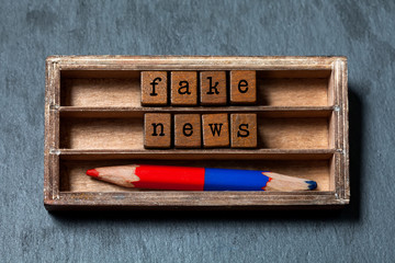 Fake news concept. Vintage box wooden cubes words phrase Fake News old style letters words, red blue pencil on gray stone textured background. Close-up, up view, soft focus