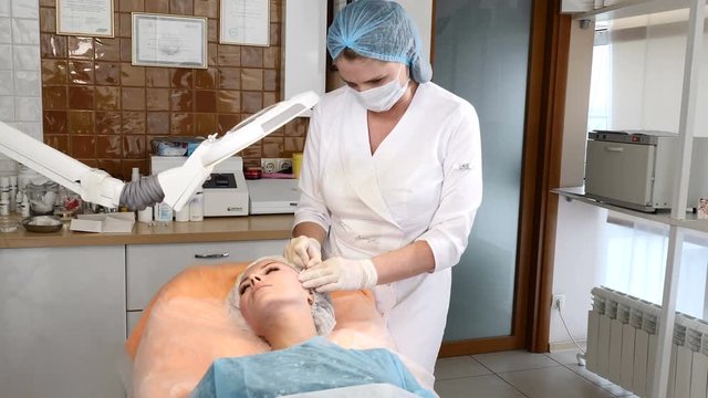 Healtcare clinic. Young female client gets thread face lifting procedure. Beautician in gloves making face anti-aging to a female face