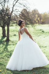 Thoughtful bride stands on the green lawn in bright summer day