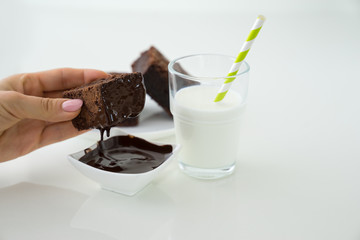 Slice of delicious homemade chocolate brownie served on white plate. Served with glass of milk with green white stripe straw. Taken on a white background.
