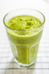 Glass with green smoothie on the kitchen table.