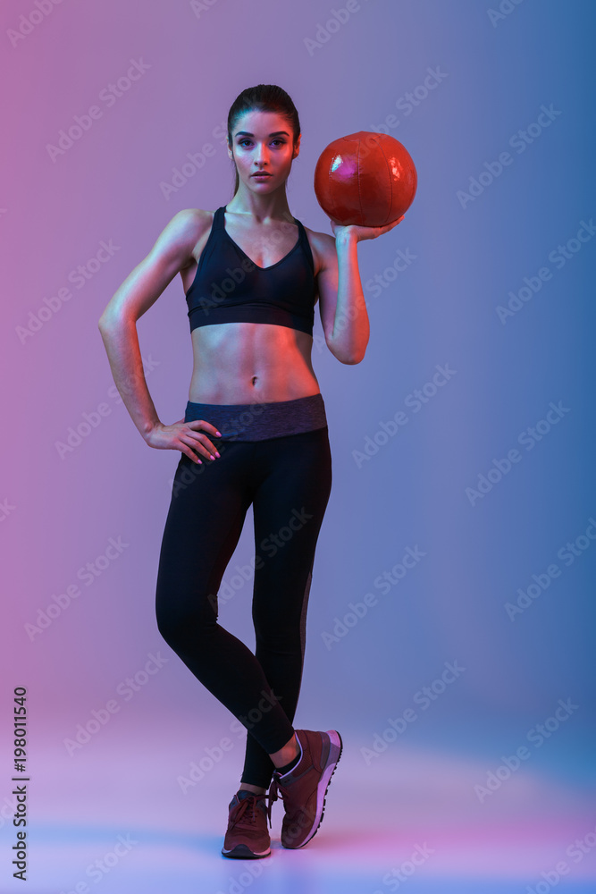 Wall mural Serious young sports woman standing with ball