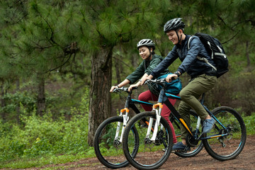 Fototapeta premium Side view of young Asian couple wearing helmets while practicing cross-country cycling