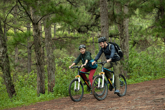 Young Asian couple enjoying cross-country cycling through woodland