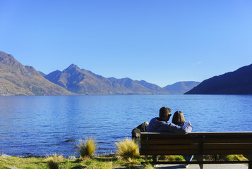 Obraz na płótnie Canvas Couple sitting on the chair in Queenstown Garden , relaxing with atmosphere of Lake Wakatipu in Autumn , Queenstown , South Island of New Zealand