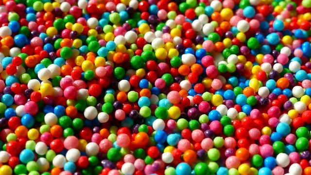 A multi-colored dragee spins on a plate. Multicolored balls. All the colors of the rainbow. Colored easter dragees. Red blue green yellow white white orange.