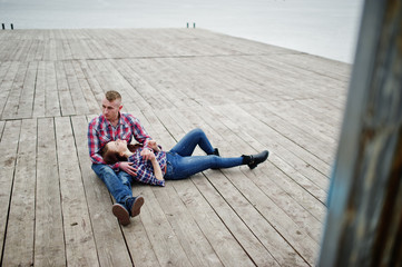 Stylish couple wear on checkered shirt in love together sitting on pier.