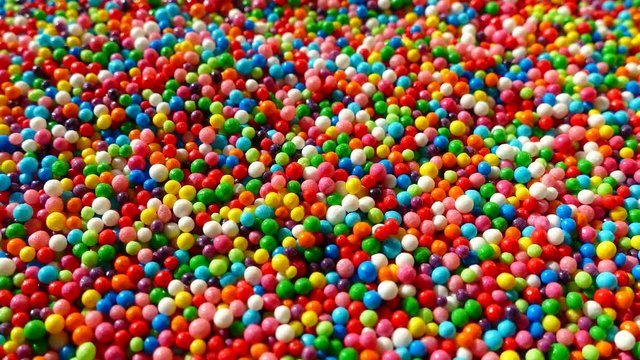 A multi-colored dragee spins on a plate. Multicolored balls. All the colors of the rainbow. Colored easter dragees. Red blue green yellow white white orange.
