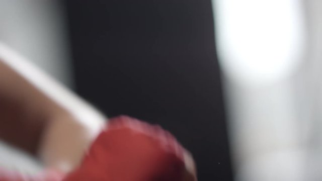 Close up shot of woman wrapping her hand with red wrist wrap, fastening and checking it before boxing workout at the gym