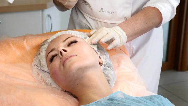 Healtcare clinic. Young female client gets thread face lifting procedure. Beautician in gloves making face anti-aging to a female face