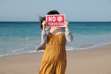 海岸で禁煙プレートを持つ妊婦  Pregnant woman who has a no smoking plate at a coast