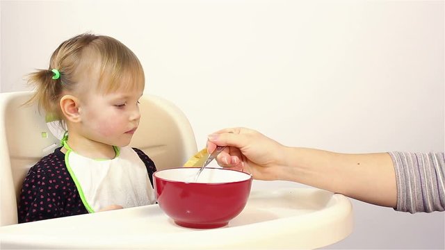 A small two-year-old girl eats porridge.