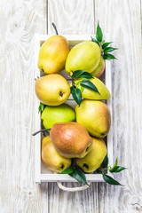 Fresh ripe pears in wooden box on light wooden background. Top view, copy space.