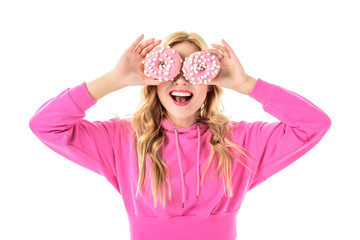 Blonde woman in pink clothes holding doughnuts in front of her eyes isolated on white