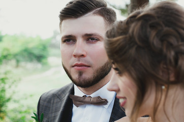 Beautiful wedding couple portrait in the forest. The bride with elegant hairstyle is standing near the bearded groom in bow tie. Hipster rustic stylish love story outdoors.