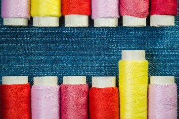 Spools of red, pink and yellow threads on denim closeup