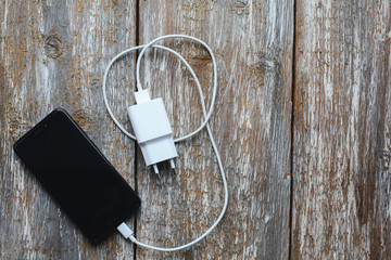 White charger and black smartphone on old wooden background. Information technology horizontal digital photo. Modern layout on vintage texture.