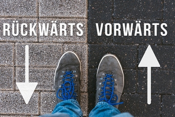 Vor einer wichtigen Entscheidung stehen &uuml;ber r&uuml;ckw&auml;rts und vorw&auml;rts in der Zukunft symbolisiert durch F&uuml;&szlig;e auf zwei unterschiedlichen Farben auf Stra&szlig;e