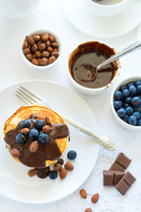 Traditional breakfast concept. Stack of pancakes with chocolate souce, blueberries and nuts on white table cloth. Selective focus