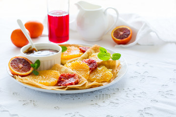 French pancakes. Crepe Suzette with caramel, oranges, blueberries, almonds and hazelnuts on white table cloth