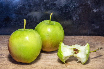 Two aplles and bitten apple on cutboard with dark background
