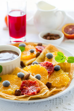 French pancakes. Crepe Suzette with caramel, oranges, blueberries, almonds and hazelnuts on white table cloth