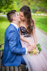 Romantic kiss of newlyweds in park on bench