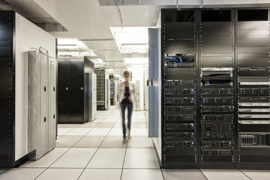 Computer server room racks with technician in background.